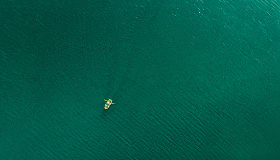 Color image depicting an aerial bird's eye view of a single rowboat on the lake, being rowed by someone. The lake is peaceful and calm in the early morning. Room for copy space.