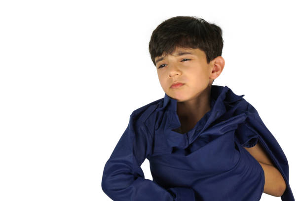 One cute Indian Asian young kid trying to take his arm out of the sleeve of his navy blue coloured kurta, which seems a bit tight or small for him. Stock image, photograph of a young Asian kid, Pranav Syal, isolated over white color backgrounds. The boy wears an irritated expression of frustration, annoyance, eyes half or part closed and a navy blue coloured Kurta pajama Pathani suit, a traditional Indian Pakistani , Pakistan or Asian dress. Front view pose. One boy only. No text, Copy space, copyspace. Expressive , facial expression , expressions in the eyes are of irritation. White background.