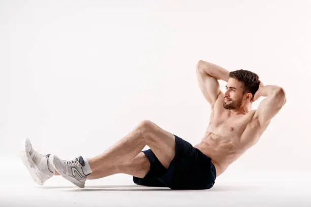 Photo of young man with a beard of a sports physique does an exercise on the muscles of the abdominal cavity on a white isolated background, the athlete goes in for sports, exercise on the muscles of the press