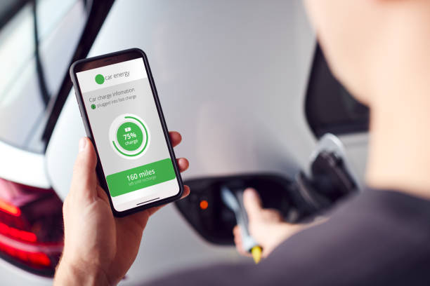 istock Man Charging Electric Vehicle With Cable Looking At App On Mobile Phone 1173292980