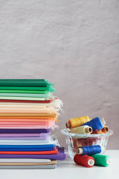 stack of colorful monochromatic fabrics and spools of thread on grey  background, space for text - patch textile stack heap imagens e fotografias de stock