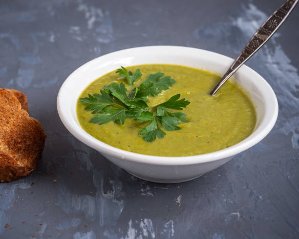 istock Pea soup mashed in a deep white plate with fresh sprigs of parsley, spoon and fried toast on a gray background 1173293987