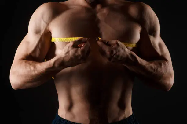 Photo of Bodybuilder with a measuring tape around his chest. Nude bodybuilder with a measuring tape around his chest isolated on black background