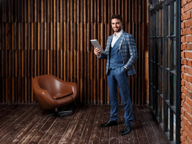 istock young successful businessman with a beard in a luxurious blue checked suit. Man works on a tablet in a loft office 1173301350
