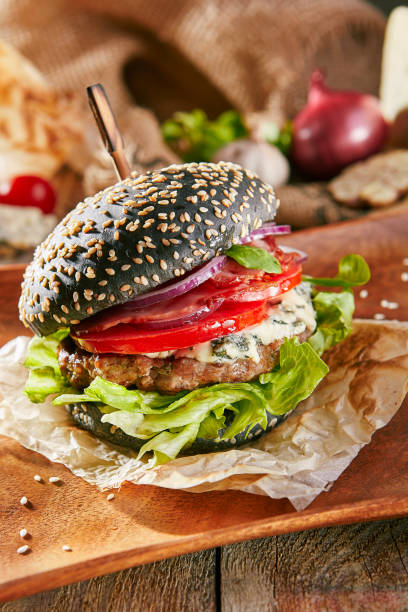 istock Burger Grill Restaurant Menu - Delicious Black Burger with Blue Cheese on Wooden Plate. Rustic Wooden Table and Ingredients on Background 1173302896