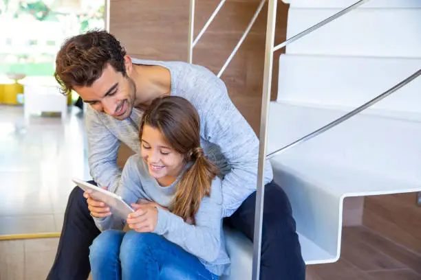 Father and daughter with tablet pc sitting in stairs at home