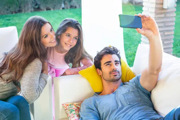 Family mother dad and daughter in garden sofa selfie with mobile phone