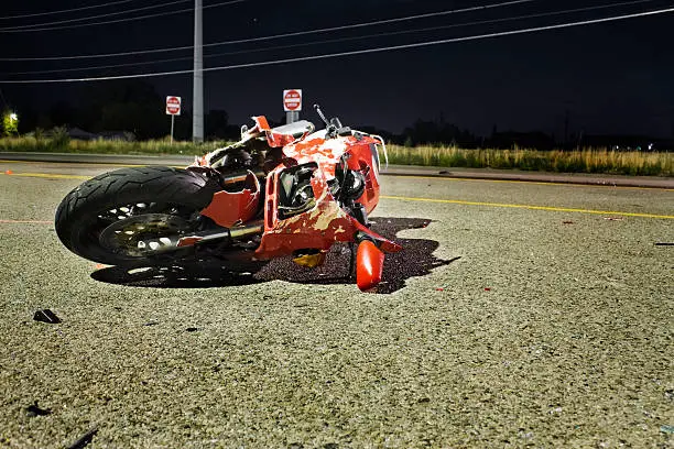 Crash scene.  Red motorcycle laying on its side on the street.  Illuminated by a overhead street light.