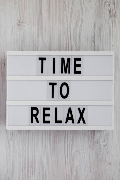 'Time to relax' words on a modern board over white wooden surface, top view. Overhead, from above. Flat lay. Close-up.