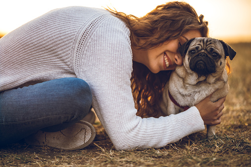 Young beautiful caucasian woman hugging with pug dog in a public park.