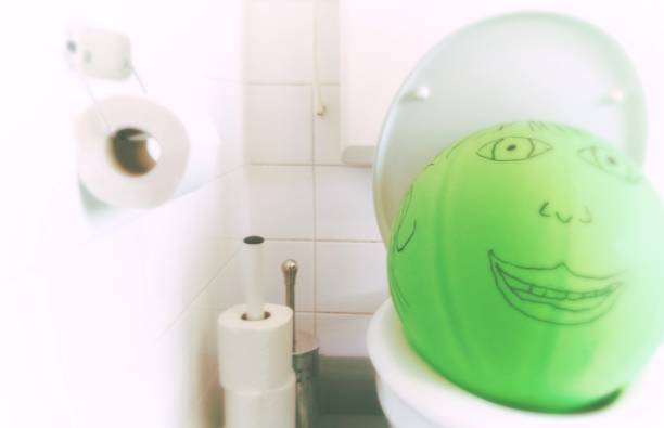 green balloon with painted face on a toilet in a white bathroom