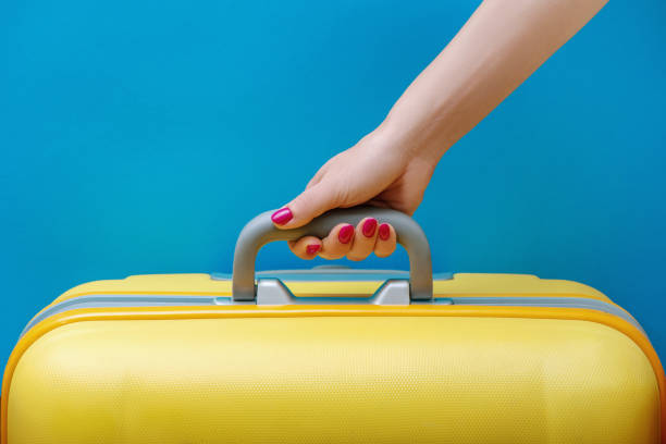 mujer sosteniendo la maleta amarilla en la mano sobre el fondo azul. - chest fly fotografías e imágenes de stock