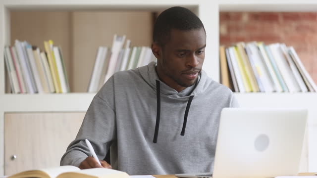 Focused african student study online on computer make notes