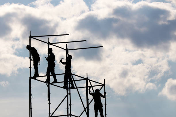 Construction workers on scaffolding Silhouettes of people working on construction site against the blue sky with white clouds factory worker silhouette stock pictures, royalty-free photos & images