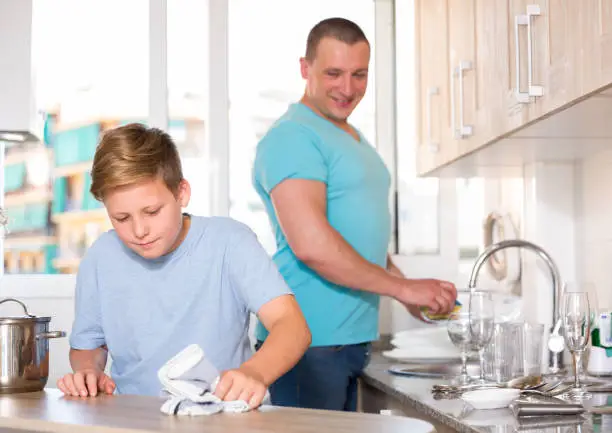 Boy and his father are helling mother and washing dishes at the home.