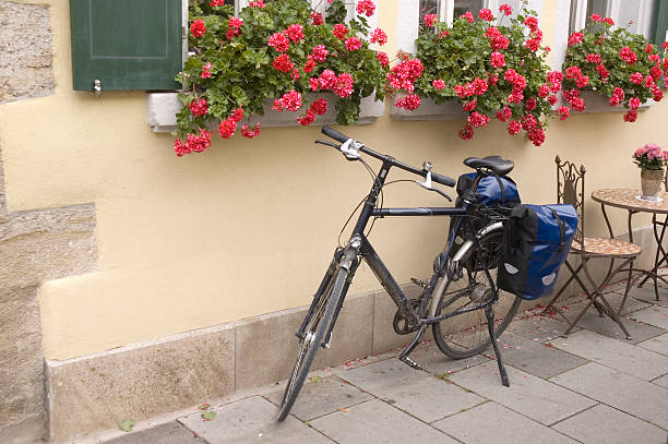 A bicycle is parked under window boxes filled with geraniums at an outdoor cafe in Rothenburg, Germany