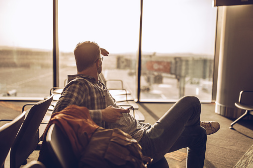 One man, gentleman sitting in waiting room on airport, using smart phone.