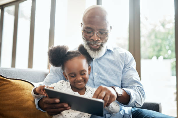 Bonding while playing in the modern age Shot of a little girl using a digital tablet with her grandfather at home grandchild stock pictures, royalty-free photos & images