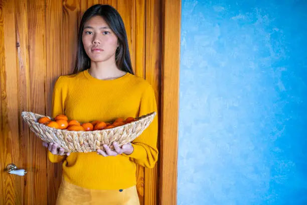 Asian woman holding oranges and tangerines basket in both hands