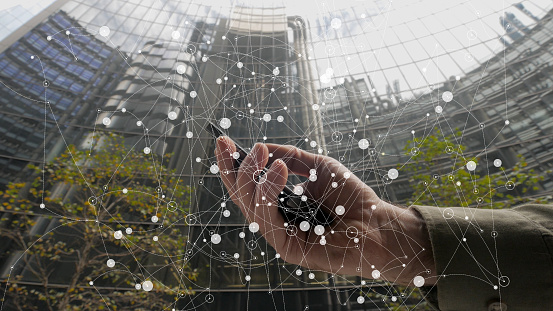 A hand holding a phone with City office background overlaid with a nodes and connectors network.