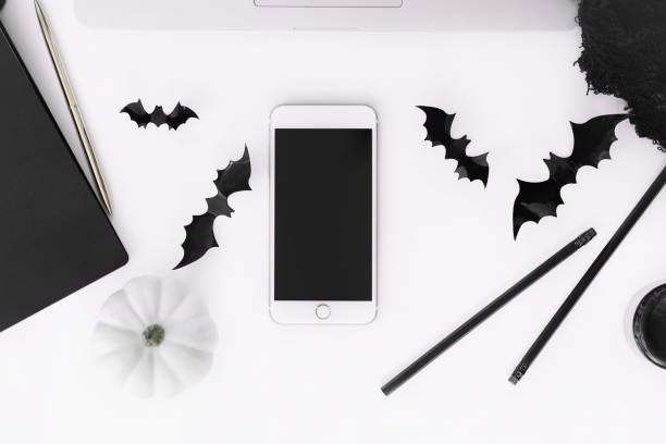 Halloween concept flat lay with pumpkins, bats and black net isolated on white background top view. Phone mockup with empty screen, laptop, candles on table. Party decoration Halloween template katt halloween stock pictures, royalty-free photos & images