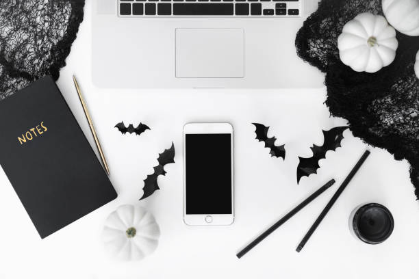 istock Halloween concept flat lay with pumpkins, bats and black net isolated on white background top view. Phone mockup with empty screen, laptop, candles on table. Party decoration 1173339015