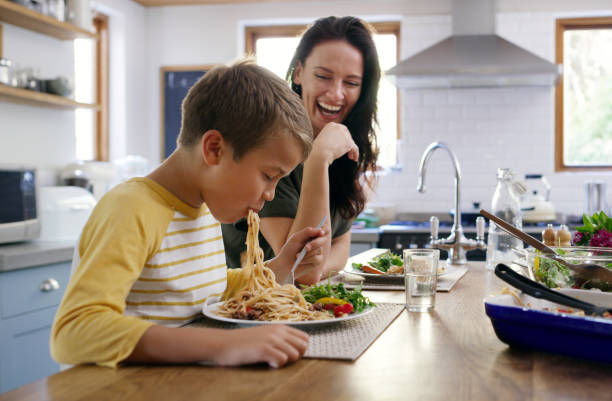 Mommy loves a boy who'll finish his food! Cropped shot of an affectionate young boy going in on his spaghetti while his mother laughs in the background kids eating noodles stock pictures, royalty-free photos & images