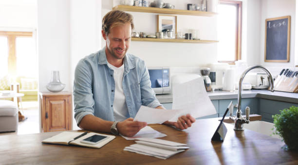 Well that turned out pretty well Cropped shot of a handsome young man looking cheerful while going through his budget at home financial bill photos stock pictures, royalty-free photos & images