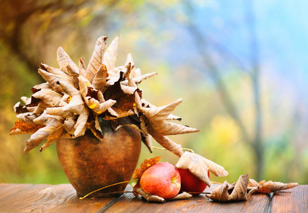 Autumn leaves in a clay pot and apple on wood floor