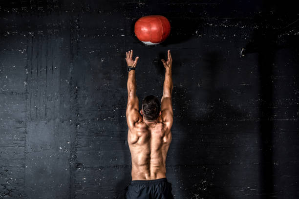 giovane forte sudato focalizzato in forma uomo muscoloso con grandi muscoli facendo lanciare palla di medicina sul muro per allenarsi allenamento hard core in palestra persone reali messa a fuoco selettiva - back against the wall foto e immagini stock