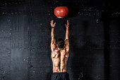 Young strong sweaty focused fit muscular man with big muscles doing throwing medicine ball up on the wall for training hard core workout in the gym real people selective focus