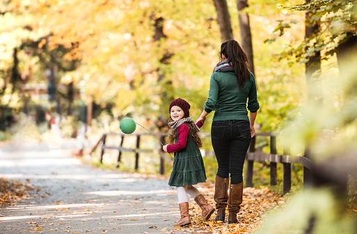 A rear view of mother with a toddler daughter walking in forest in autumn nature, holding hands.