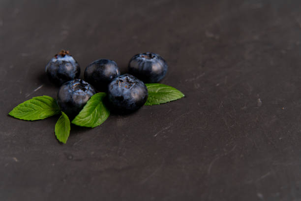 blueberries with green leaves lie on dark black background. Copy space