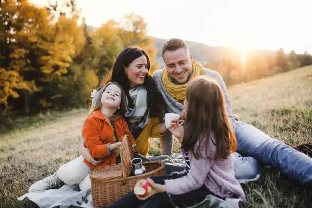 Photo of A young family with two small children having picnic in autumn nature at sunset.
