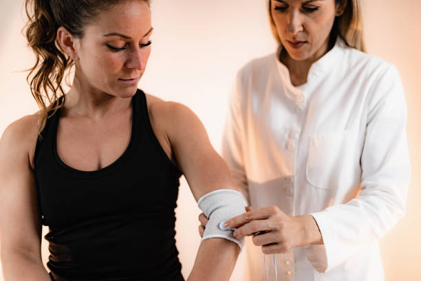Elbow Physical Therapy with TENS Electrode Brace Pads, Transcutaneous Electrical Nerve Stimulation. Therapist Positioning Electrodes onto Patient's Elbow