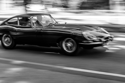 Jaguar E-Type driving at high speed on a road through a forest near Baarn in Utrecht, The Netherlands during a sunny summer day.