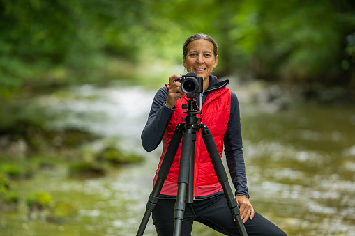 telephoto shot of professional outdoor photographer smiling female woman shallow depth of focus on smiling woman with camera tripod closer view