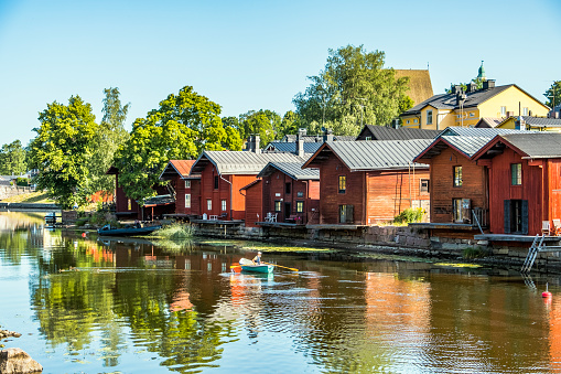 Old Porvoo, Finland: August 6, 2019: Bearded man rowing canoe down river in front of famous Old Porvoo red buildings with reflections in still water
