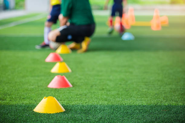 istock Selective focus to marker cones are soccer training equipment on green artificial turf with blurry coach is training kid players background. 1173351749