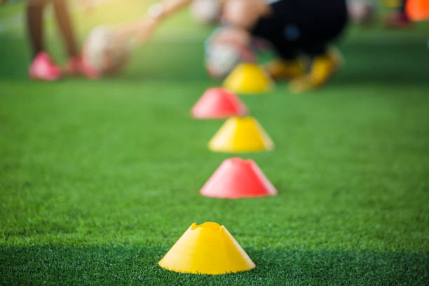 istock Selective focus to marker cones are soccer training equipment on green artificial turf with blurry coach is training kid players background. 1173351773