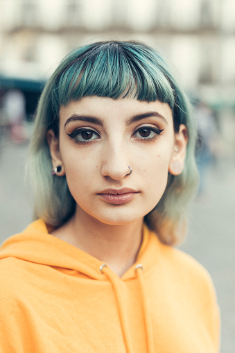 Close up portrait of young woman with green hair and a nose ring.