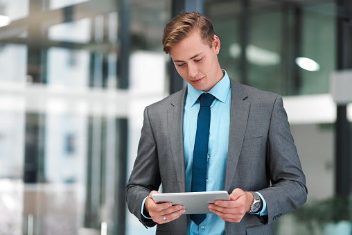 Cropped shot of a handsome young businessman standing alone in his office and using a tablet