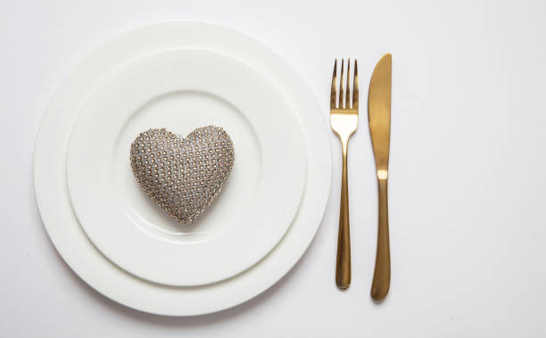 Wedding anniversary dinner table setting, Gold fork and knife on white set of dishes isolated, white background, top view