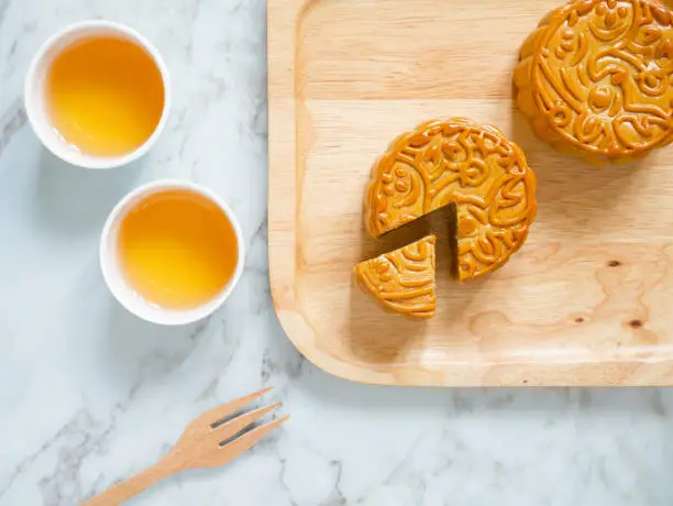 Photo of Mooncakes on a wooden plate with cups of tea