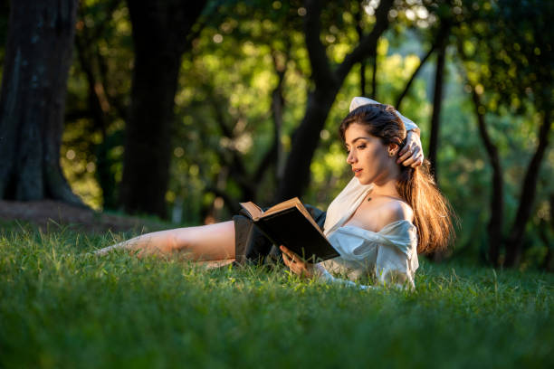 istock Beautiful woman relaxing in grass and reading a book 1173360358