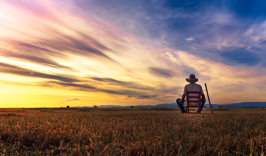 farmer sitting on a chair looking at the field and sunset