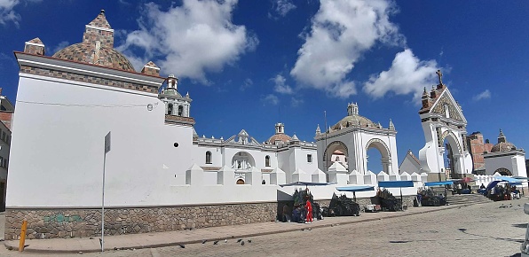 Scene Of Souvenir Vendors Displaying Different Type Bolivian Souvenir For Sale, Tourist Walking In And Out Of Basilica Of Our Lady Of Copacabana During The Day In Bolivia South America