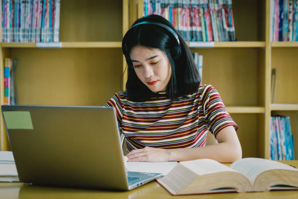 istock Young Asian woman student study and take notes with book in library. Female university student sitting at table doing assignments in college library. Student using laptop and learning online. 1173361885