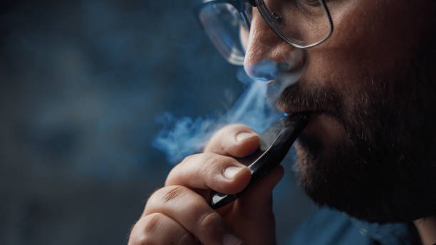 Man smokes new Vape Pod System, inhales and exhales vapor of electronic cigarette, vaping concept stock photo