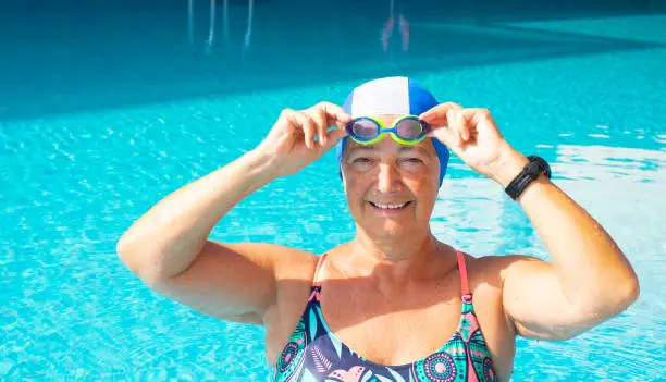 An elderly woman who enjoys the swimming pool. Nobody else with her. Healthy lifestyle by doing physical activity. Sunny day and transparent water